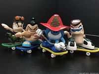 Four Tech Deck Dudes skateboard figures posed on skateboards in black background