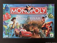 Top of game box showing Disney Pixar Monopoly branding and characters from Finding Nemo, Toy Story, Cars, Ratatouille, The Incredibles, and Monsters Inc