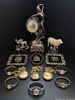 Front view of all items showing decorative clock, figurines, framed plaques, watches, and pocket watches arranged on black surface.