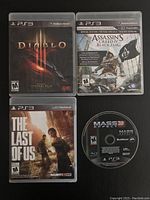 Four PS3 games arranged with covers Diablo 3, Assassin's Creed IV Black Flag, The Last Of Us, and the Mass Effect 3 disc.