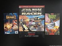 View of Rayman 2, Star Wars Episode I Racer, and Thunder Spirits manuals placed side by side on black surface.