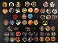 Top view of 57 assorted vintage Pogs and Slammers arranged neatly on black background showing various designs and scattered groupings.