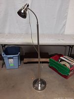 Full view of the chrome floor lamp standing upright with flexible gooseneck lamp head angled downward. The lamp shows no visible damage and has a round weighted base.
