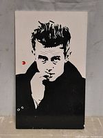 Frontal image of the monochrome James Dean portrait, black and white with high contrast, signature mark visible in the composition.