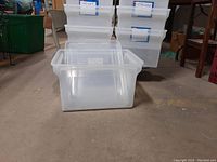 Eighteen clear plastic bins stacked on a dolly, with some lids visible on top and one bin in front showing internal dimensions.