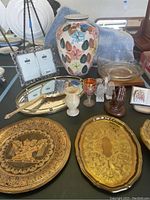Full view of the lot showing all items arranged on a table including vases, trays, plates, hand mirrors, salt and pepper shakers, praying hands sculptures, photo frame, and porcelain book box.