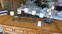 Long black metal mantle piece candelabra with five white pillar candles displayed on wooden surface.
