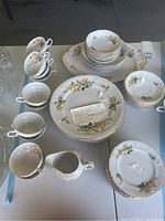 Top view of entire china set including plates, bowls, cups, saucers, creamer and lidded dish showing yellow rose floral pattern and gold trim.
