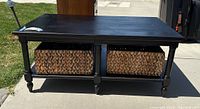 Side angle photo showing black wood coffee table with turned legs and two large woven wicker baskets in lower shelf.
