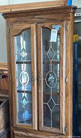Full front view of curio cabinet showing oak wood frame with decorative glass doors and mirrored interior.