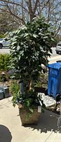 Full view of the faux tree in decorative pot positioned outdoors with visible leaves, trunk, pot and attached metal flower sign.