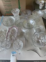 Front view of glassware items showing multiple clear glass dishes, bowls, vase and candy dishes with detailed cut patterns on a table surface.