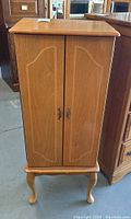 Closed view of the wood jewelry cabinet showing carved details on the doors and four curved legs.