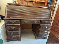 Full front view of the dark wood roll top desk showing nine drawers and closed roll top covering the workspace.