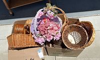 Top view of multiple wicker baskets including a prominent one decorated with pink satin bows and lace flowers inside a cardboard box