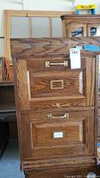 Front view of wooden filing cabinet showing two drawers with brass hardware and label holders, visible scratches.