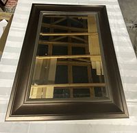 Bronzy/brown rectangular mirror with brown plastic frame and beveled mirror surface, shown laying horizontally