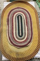 Small oval rag rug with concentric ovals in red, burgundy, cream, green, and beige colors with some dirt marks and slight wear