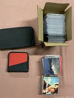 Overview of two cloth CD storage containers (one black, one red and black) and a cardboard box filled with empty jewel cases, along with some loose CDs and cases.