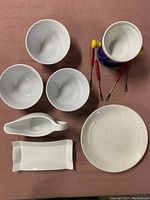 Top view of fondue pot with forks inside, three bowls surrounding, small gravy boat and rectangular tray, and decorative plate all arranged on a surface.