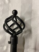 Close-up of a black metal basket-style finial with tightening bolt attached
