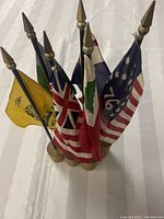 Cluster of six small flags on wooden block base featuring colonial and historical designs including the 1776 American flag and a yellow Gadsden flag.