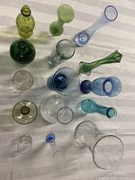 Top-down view of all 14 glass vases, bottles, and glasses in various colors including clear, green, blue, and yellow.