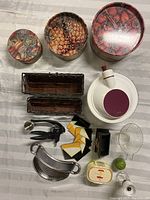Photo showing three decorative round cookie tins, two rectangular kitchen organizer boxes, salad spinner, pot strainer, a set of coasters with holder, bento box, lime salt shaker, condiment mill, garlic press