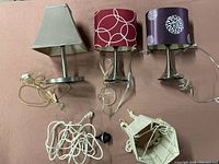 All three table lamps with distinct fabric shades and cords visible, plus hanging cord and hanging lantern shade on floor