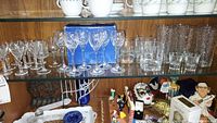 Shelf display showing multiple types of stemware including Waterford cordial glasses and other clear crystal glasses.