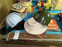 Photo showing three costume hats on a game table, includes white AT&T hard hat, tan safari hat, and olive green military helmet. Board game with Nightmare on Elm Street visible underneath.