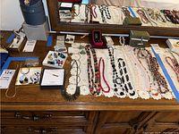 Wide view of dresser top showing multiple necklaces laid on white lace runner and assorted earrings near mirror