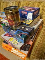 Multiple boxed board and card games stacked, including Sports Chronology, Challenger, a large tin container with French wine label, Cranium game box.