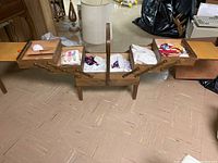 Open expanding wooden sewing box showing multiple zigzag hinged trays filled with various sewing supplies including threads, scissors, needles, and other sewing notions.