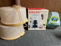 Two stackable Tupperware containers with lids, Krups Espresso Bravo coffee maker box, and Fruit & Vegetable wash item on carpeted floor