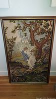 Front view of the framed needlepoint artwork of children on a swing under a tree.