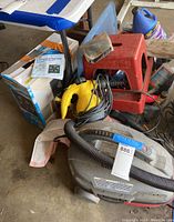 Photo showing wet/dry vacuum cleaner, yellow blower, gallon jug of soap, red step stool, cleaning rags, and boxes with accessories.