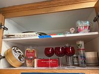 Photo of a cabinet shelf with red glass stemware, decorative tins, and glass tumblers with holiday designs.