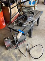 Photo showing Sears Craftsman belt sander on the router table with air compressor on the floor.