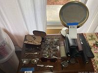 Multiple prescription eyeglasses and sunglasses laid out on a table with various eyeglass cases and a magnifying mirror with light.
