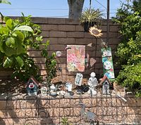 Full view of metal fencing panels and assorted garden decorative items arranged on a ledge and ground, including hanging sunflower planter with air plant and colorful garden plaque.