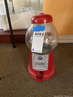 Front view of the glass bubblegum machine with coin slot and turn handle visible on the red metal base.