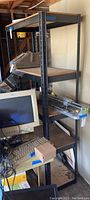 Full view of black metal frame shelf with wood inserts, showing four shelves and some surrounding items in a storage space.