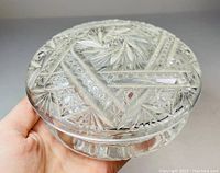 Crystal trinket box held in hand showing detailed brilliant cut patterns on lid and base.