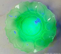 Plate glowing bright green under UV light showing frosted rose and leaf design.
