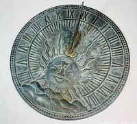 Front view of the sundial showing sun face and Roman numerals with gnomon shadowing near 12 o'clock.