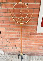 Full view of the copper ornamental twirling garden sprinkler showing the circular top with spiral interior and lower semi-circular arms mounted on a long copper pole with four-spike metal base.