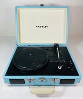 Open portable turntable showing platter, tonearm, speed options and controls, with white interior lid lining featuring Crosley logo.