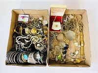 Overhead view of two boxes filled with assorted jewellery pieces including bracelets, rings, necklaces, watches and brooches.