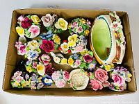 Box containing multiple fine bone china flower arrangements and bouquets with various colors and styles, including an oval basket with floral handles.